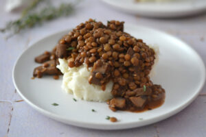 Mijoté de lentilles et champignons servi sur une purée de pommes de terre onctueuse, garni de thym dans une assiette en céramique.
