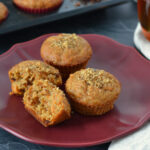 Muffins aux carottes, dattes et thé chaï (ultra moelleux) 3 muffins aux carottes dans une assiette rouge avec un thé chaï en arrière plan. Focus sur un muffin aux carottes coupé en deux montrant les morceaux de dattes et la texture fondante et moelleuse du muffin.