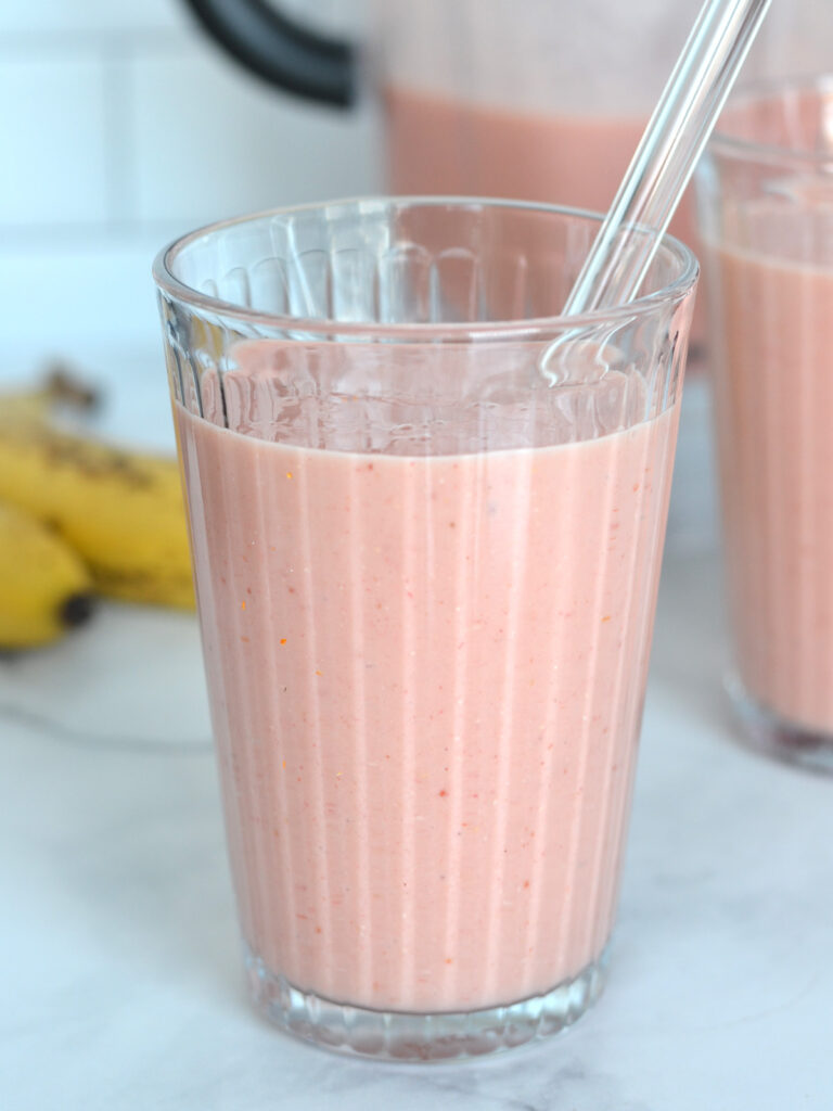 Verre de smoothie aux fruits avec des bananes en arrière plan