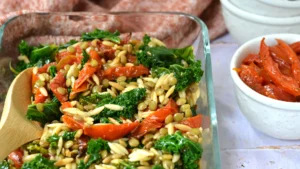 Salade de lentilles et tomates confites, kale et orzo dans un grand plat de verre et cuillère de service, bol de tomates confites sur le côté.