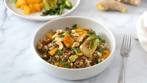 Une salade de lentilles miso gingembre dans un grand bol en céramique avec à l'arrière, des bok choy grillés, racine de gingembre et des suprêmes d'oranges.