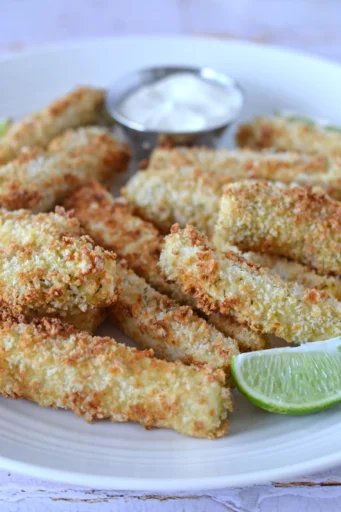 Bâtonnets de tofu panés au jus de cornichon dans une assiettes avec lime et un contenant de sauce citron et aneth.