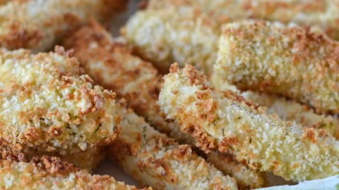 Bâtonnets de tofu panés au jus de cornichon dans une assiettes avec lime et un contenant de sauce citron et aneth.