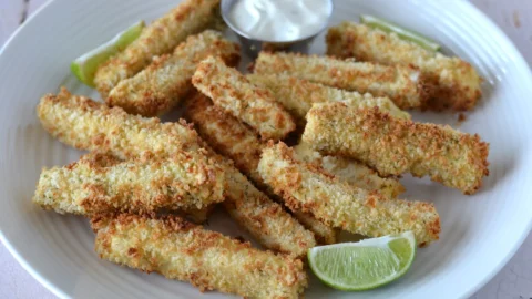 Bâtonnets de tofu panés au jus de cornichon dans une assiettes avec lime et un contenant de sauce citron et aneth.