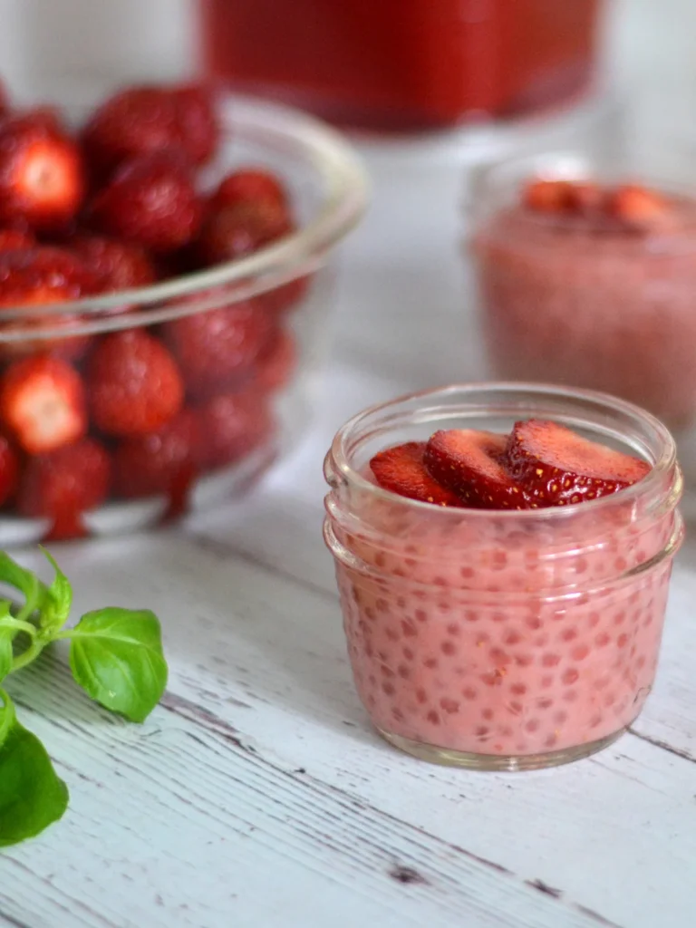 Pouding de tapioca lait de coco et fraises servi dans un pot Masson avec en arrière plan fraises fraiches et fraises en purées. 