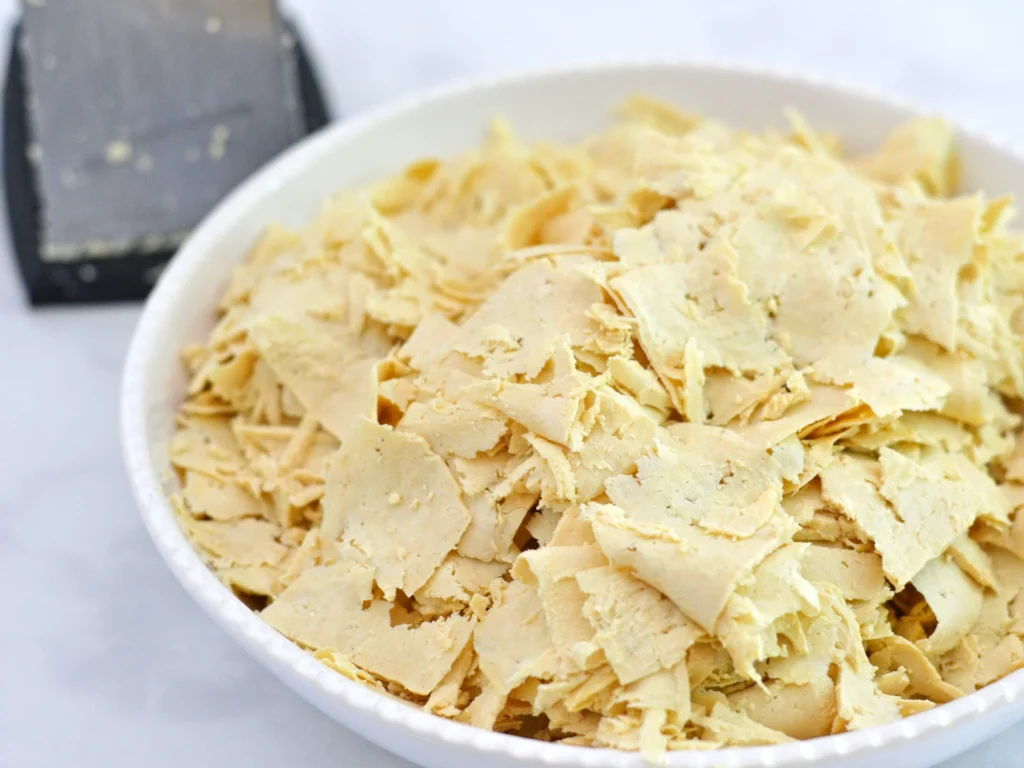 Bol de tofu râpé avant la cuisson avec, à l'arrière, la râpe utilisée pour la préparation. 