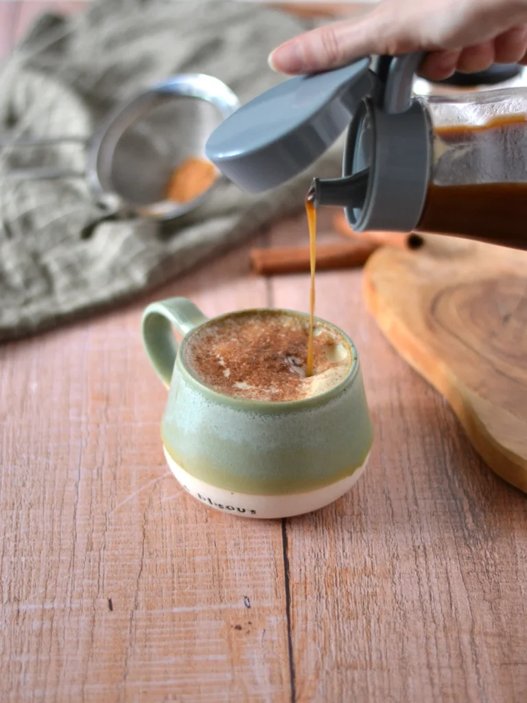 Sirop à la citrouille épicée maison Latté à la citrouille dans une tasse avec une main qui verse du sirop à la citrouille maison.