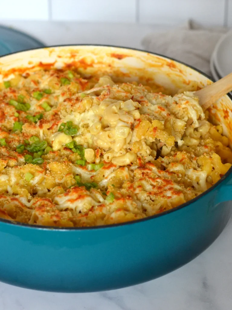 grand chaudron bleu contenant du macaroni au fromage à la courge avec une cuillère de bois qui vient prendre une portion